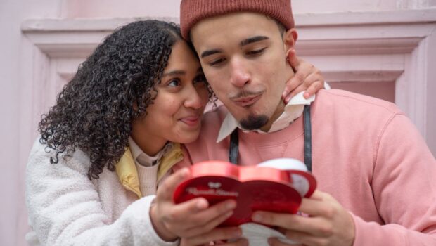 Loving young Hispanic couple eating chocolates on street and cuddling