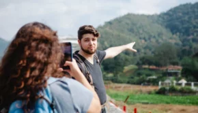 Female taking photo of traveler pointing at green hill in countryside